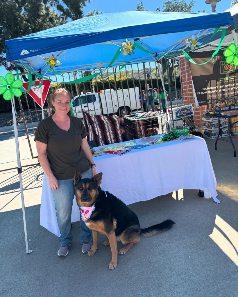 Smiling woman with a dog at Snuggle Puppy Hotel booth showcasing their pet care services in Redlands & Rialto, with personalized attention for every dog and a safe, clean facility
